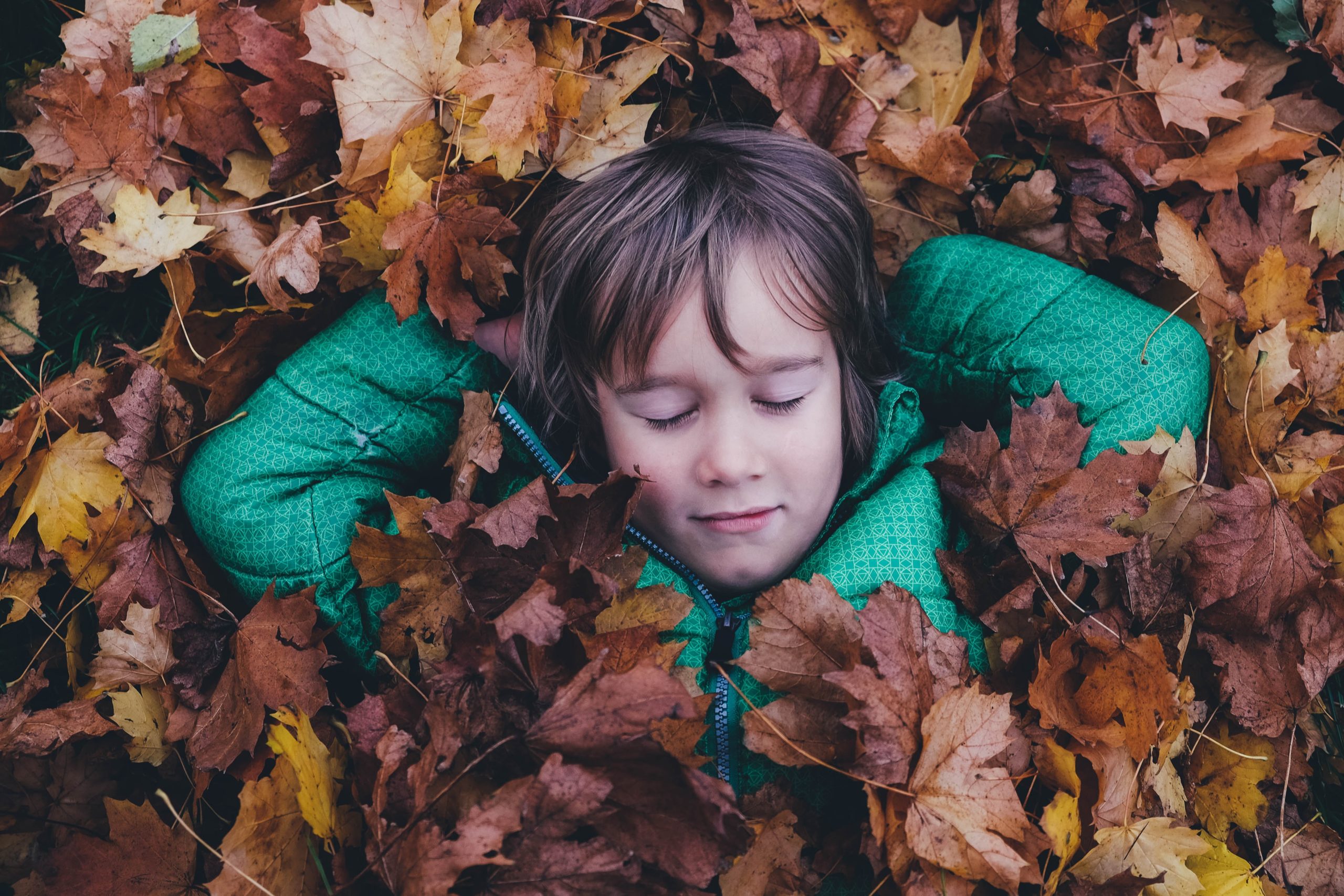 A little boy laying in a pile of leaves enjoying his time away from scheduled activities in Katy, TX 77494