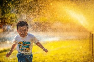 A little boy running through the sprinkler enjoying his family time in Katy, TX 77494