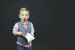 A little boy holding open a book with a surprised look on his face. Represents the need for family counseling to learn parenting tips in Katy, TX 77494